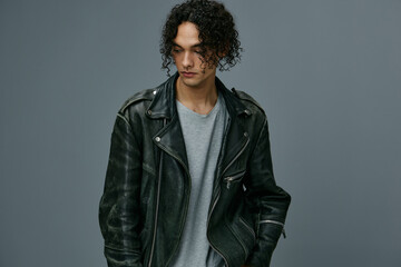 Fototapeta premium Serious adorable stylish tanned curly man leather jacket looks aside posing isolated on over gray studio background. Cool fashion offer. Huge Seasonal Sale New Collection concept. Copy space for ad