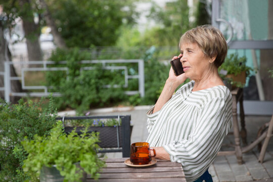 happy senior woman talking on cellphone in the garden near the house in summer.