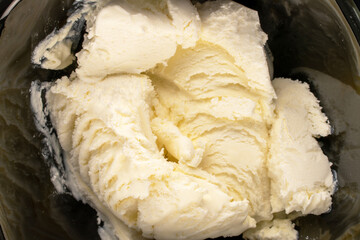 Several scoops of cold white ice cream in a black ceramic bowl, macro, top view.