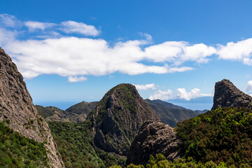 Obraz premium Massive volcanic rock formations in Garajonay National Park seen from Roque de Agando, La Gomera, Canary Islands, Spain, Europe. Hiking trail over hills covered by forest and tropical fauna in summer