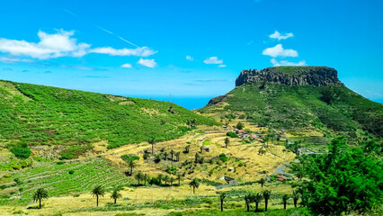 Panoramic view on massive volcanic plug Fortaleza de Chipude overlooking western coast of La Gomera, Canary Islands, Spain, Europe. Village in valley embedded lush green hills. Road to Valle Gran Rey