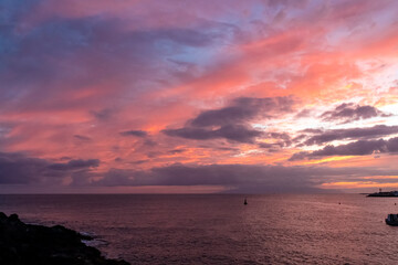 Obraz premium Romantic sunset over the sea in summer seen from lookout Cypelek Los Cristianos, Tenerife, Canary Islands, Spain, Europe. Vibrant colours of the clouds. Vacation vibes on the Atlantic Ocean. Awe