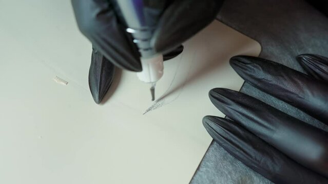 female hands in black gloves with a tattoo machine draw eyebrows on a silicone mat. permanent makeup master training. tattoo training. eyebrow permanent makeup training