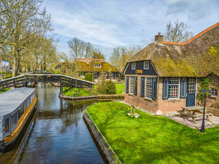 Fototapeta na wymiar Canal side thatched roof houses, bridges and boat in the fairy tale village of Giethoorn, Netherlands
