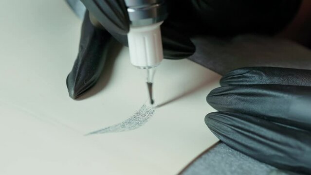close-up of female hands in black gloves with a tattoo machine draw eyebrows on a silicone mat. permanent makeup master training. tattoo training. eyebrow permanent makeup training