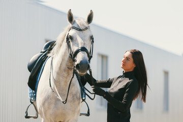 Obraz premium Young charming woman walking with white horse in summer warm day at country estate. Lifestyle mood. Concept of nature, animal, care, sport