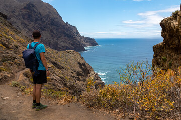 Backpack man on hiking trail from Afur to Taganana with scenic view of Atlantic Ocean coastline and Anaga mountain range, Tenerife, Canary Islands, Spain, Europe. Looking at Cabezo el Tablero crag