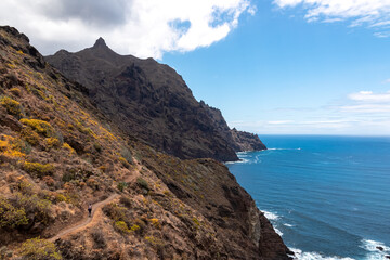 Backpack woman on hiking trail from Afur to Taganana with scenic view of Atlantic Ocean coastline and Anaga mountain range, Tenerife, Canary Islands, Spain, Europe. Looking at Cabezo el Tablero crag