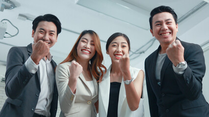 Group of happy young Asian employees raising their hands to celebrate business success.