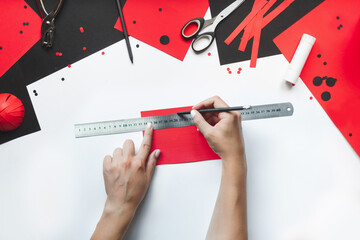 How to make paper red and black ladybug toy with children at home. Step by step instructions. Hands making DIY summer project. Step 3. On sheet of red paper 15 cm long, draw 10 lines 1 cm wide