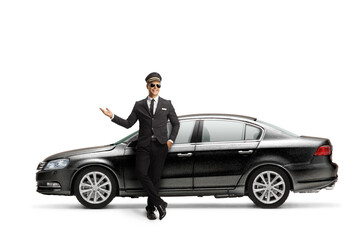 Chauffeur in a black suit showing with hand and leaning on a black car