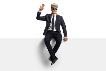 Pilot in a uniform sitting on a blank panel and waving at camera