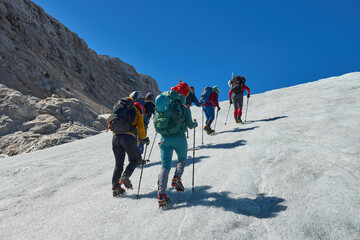 mixed gender and age group of climbers hiking up a steep glacier with crampons and poles in the...