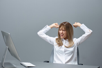 Overjoyed pretty blonde businesswoman worker freelancer using desktop computer raise hands up celebrating win in gray modern office. Remote Job, Technology And Career Profession Concept. Copy space