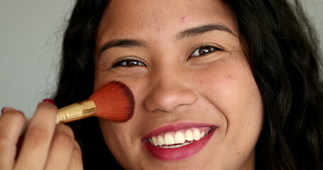 Obraz premium Casual Latina Hispanic woman applying make-up brush, looking at camera