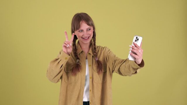 Cheerful blonde woman with pigtails making selfie on mobile in the green studio