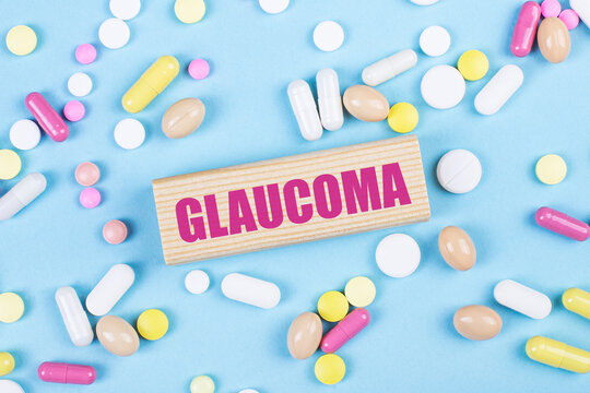 On a blue background, multi-colored pills and a wooden block with the text GLAUCOMA. View from above. Medical concept