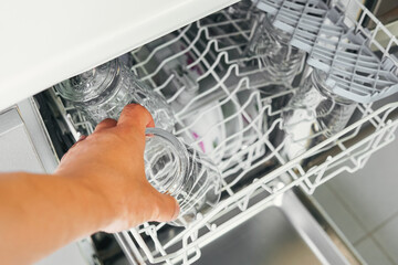 Aerial image of hand placing a glass in the automatic dishwasher in your kitchen. Hand of unrecognizable person placing a glass in the dishwasher to carry out his homemaker household chores.