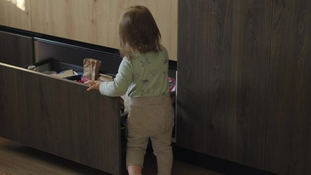 Curious baby girl exploring the drawer in the kitchen and selecting food. Childcare concept. Baby development. Baby care.