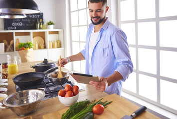 Man following recipe on digital tablet and cooking tasty and healthy food in kitchen at home - 519609048