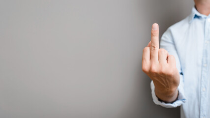 Caucasian man in shirt shows an obscene gesture, middle finger of hand rude sign on gray...