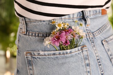 Woman with beautiful tender flowers in back pocket of jeans outdoors, closeup