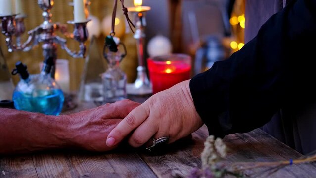 magic session, Female Fortuneteller or esoteric Oracle performs spell ritual using charmed amulet of male client's hand, candles are burning, incense is being smoked, attributes of occultism