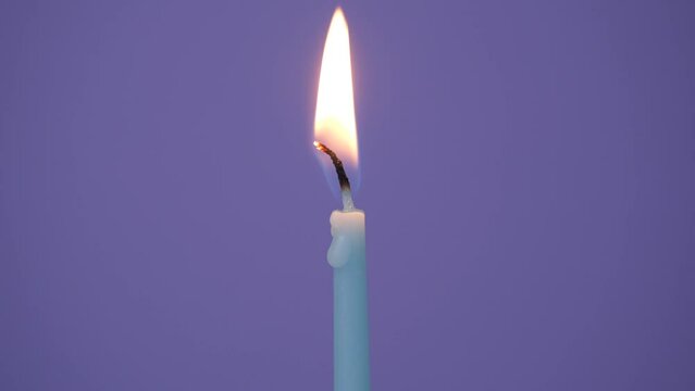 One blue cake candle burning on a purple background. Close up on blow out cake candle. Full HD resolution slow motion happy birthday or one year anniversary video banner