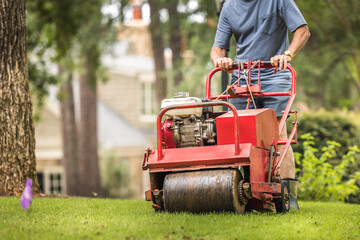 Man using gas powered aerating machine to aerate residential grass yard. Groundskeeper using lawn...