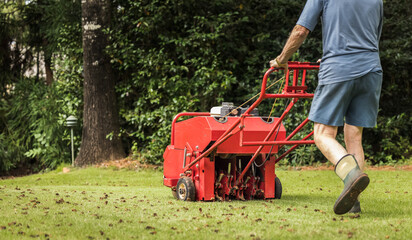Man using gas powered aerating machine to aerate residential grass yard. Groundskeeper using lawn...