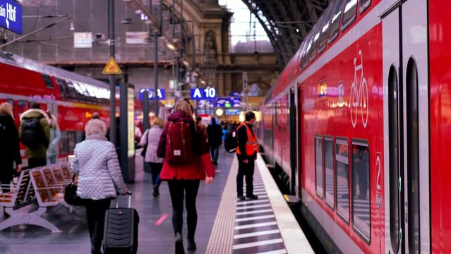 modern red train of Deutsche Bahn on platform of Frankfurt am Main station, passengers with luggage and backpack go to board train, concept of boarding travelers in cars, Frankfurt - January 2022