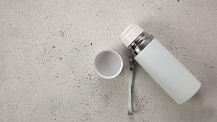 White thermos for drinks for travel and sports on a light background, top view, blank space for text