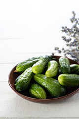fresh cucumbers in a bowl on a white wooden background, lavender in the background, vertical format