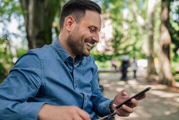 Cheerful professional text messaging on mobile phone while sitting at public park.