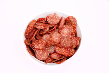 Obraz premium Salami chips, meat snacks in a bowl, isolated. Salami slices, top view, close-up. Packshot photo for package design.