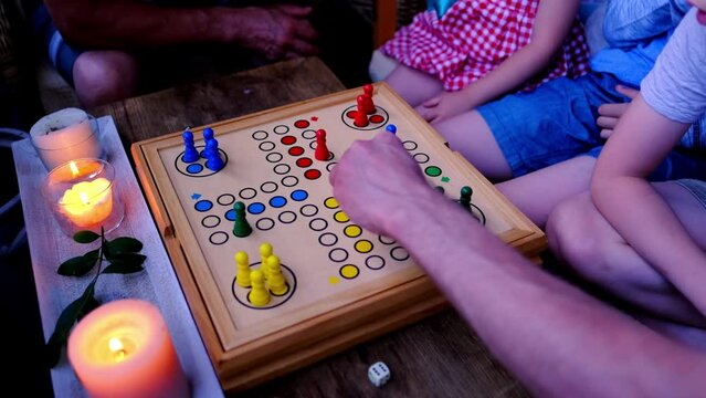 family in evening by candlelight play together, children and adults roll dice and move colorful figurines, concept of learning rules of game, board games for whole family