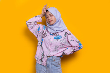 portrait of stressed tired sick asian muslim woman with headache on yellow background
