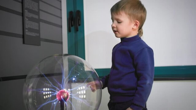 happy little male child touching a plasma ball with his hand creating electric waves, science and education