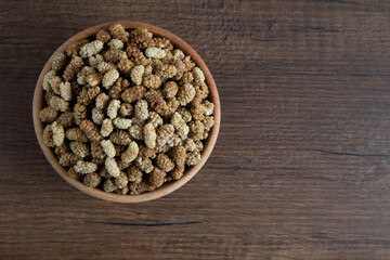 Bowl full of dried mulberry on a wooden background
