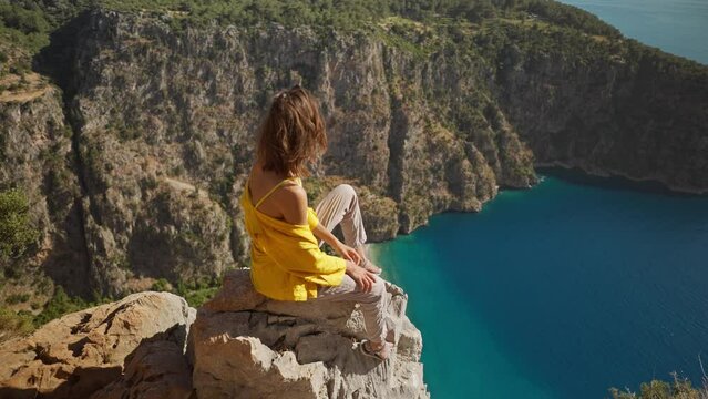 aerial Young happy woman traveler with blowing hair enjoying beautiful view of Butterfly Valley from edge of cliff on mountain top, Butterfly Valley in city of Oludeniz, Fethiye in western Turkey