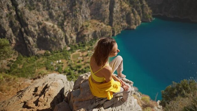 Young happy woman traveler with blowing hair enjoying beautiful view of Butterfly Valley from edge of cliff on mountain top, Butterfly Valley in city of Oludeniz, Fethiye in western Turkey