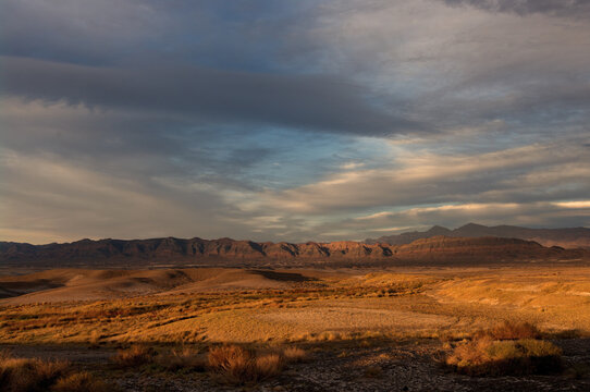 Landscape image taken at Tecopa in the Mojave Desert, California. The photo shows sunset clouds, a mountain range, and badlands. Tecopa is known for its natural warm springs.