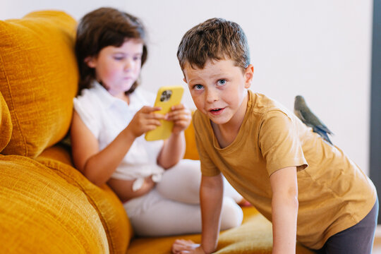 Boy with a parakeet on his back near sister on the smartphone