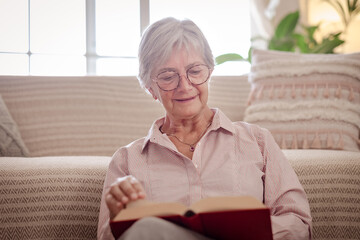 Attractive senior woman sitting on the floor at home while reading a book