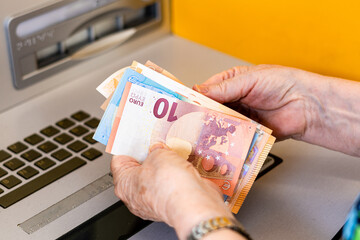 Close-up, woman's hands counting euro bills at the ATM.
