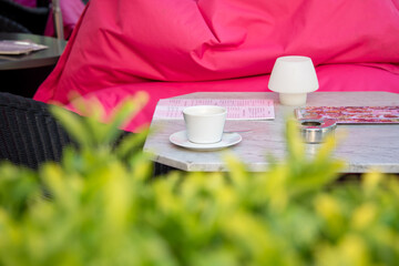 Fototapeta na wymiar Cup of coffee on outdoor cafe table. Outdoor restaurant or cafe table with coffee cup surrounded with green plants in summertime.