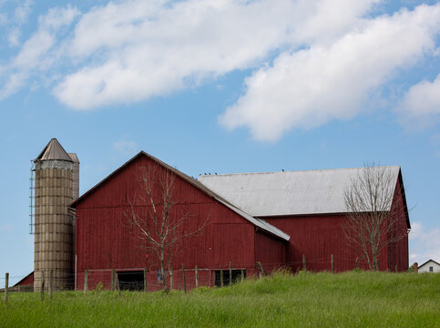 Red barn with a silo on a hill with a blue sky in the background