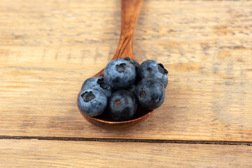Blueberries on a wooden spoon over a wooden background.