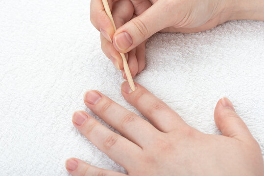 Young woman pushes back the cuticles on her nails with an orange stick.