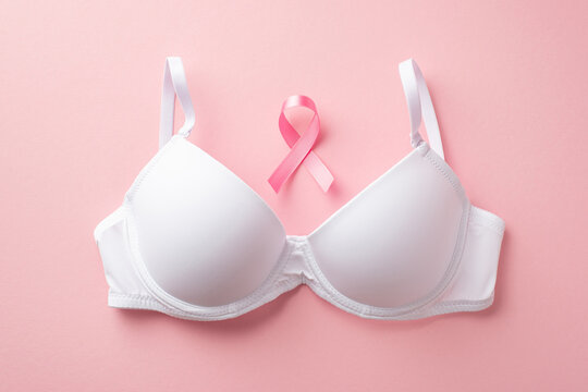 Top view photo of pink ribbon symbol of breast cancer awareness and white brassiere on isolated pastel pink background